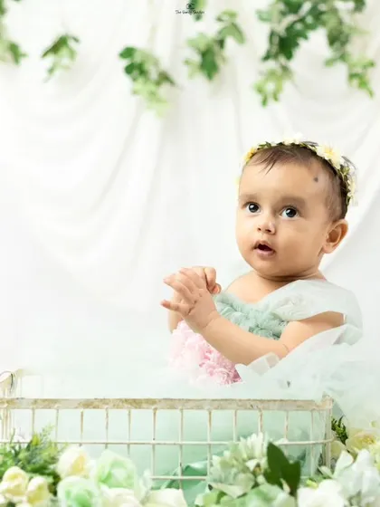 A sweet portrait of a baby girl in a wire basket, surrounded by flowers, as part of her first birthday celebration shoot.
