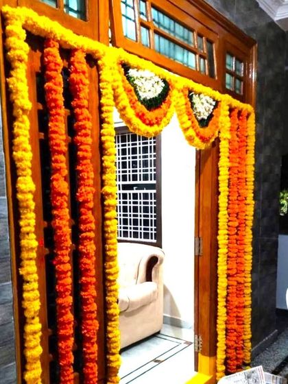 A traditional marigold flower decoration for a housewarming. The door is framed with garlands of yellow and orange marigolds and white flowers.