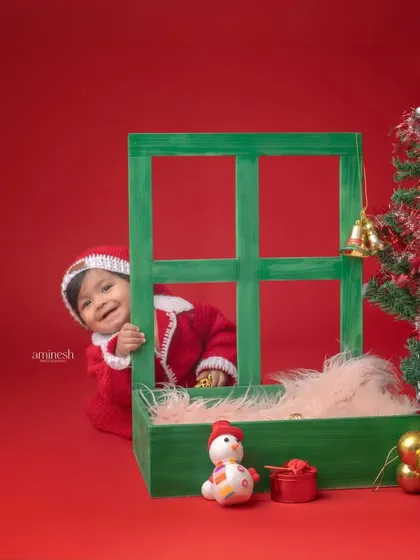 A playful peek-a-boo moment from a Christmas photoshoot. This little Santa peeks out from behind the window prop with a mischievous smile, creating a fun and candid shot.