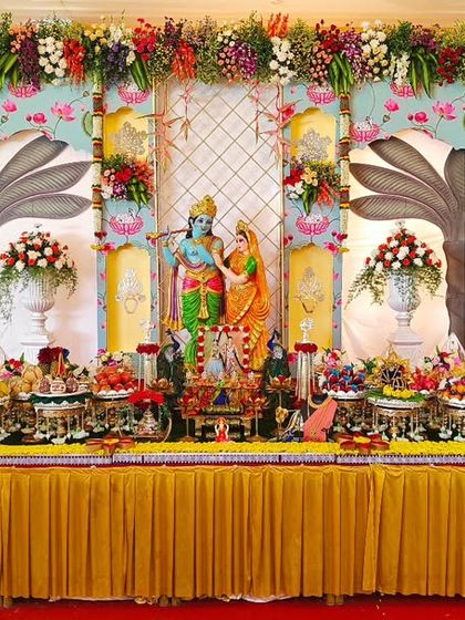 A grand engagement stage with a Krishna and Radha theme. The backdrop, floral arrangements, and extensive plate display all came together to create a divine setting.