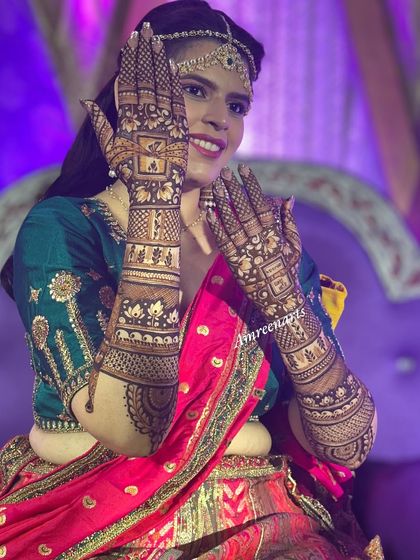 A joyful bride posing for the camera, her hands framed to showcase the intricate bridal henna.