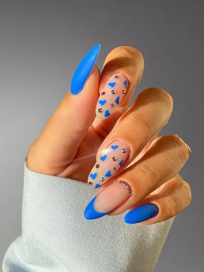 A playful blue French manicure with matte blue tips, accented with tiny blue hearts and rhinestones on a nude base.