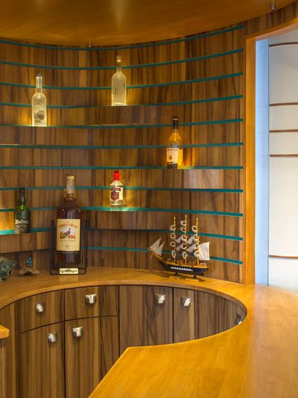 A custom-built bar area in the Outré House featuring curved wooden paneling and glass shelves. The design maximizes storage and function while maintaining the home's signature fluid aesthetic.