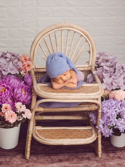 A sleepy newborn boy in a blue knit hat, posed sweetly on a miniature chair surrounded by flowers. This shows our creative use of props and color coordination.