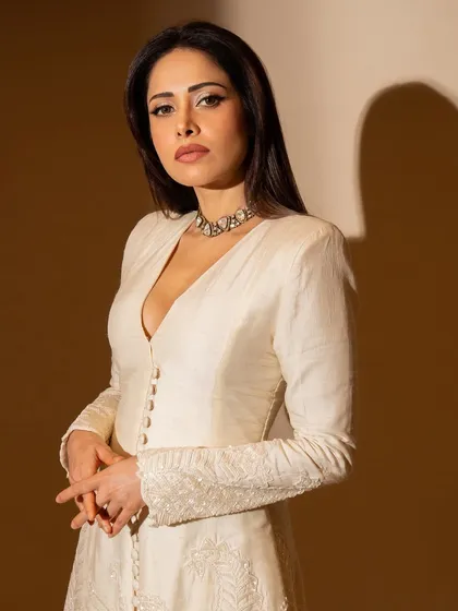 A full-length shot of this elegant ivory Anarkali-style suit on Nushrratt. The button-down front and long sleeves give it a very sophisticated feel.