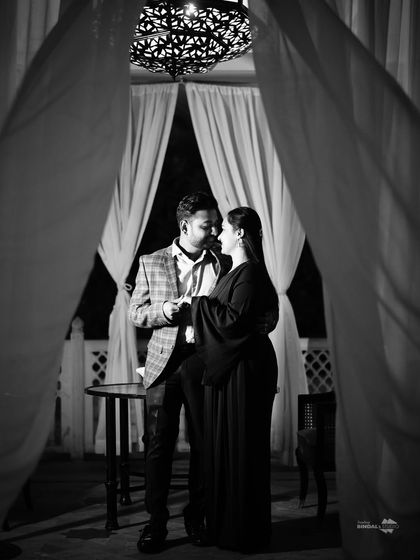 A timeless black and white portrait framed by soft curtains. This intimate shot uses shadows and light to create a classic, romantic mood perfect for a pre-wedding album.