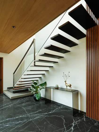 The main staircase is designed as a sculptural element, with floating wooden treads set against a backdrop of dark marble flooring and a timber-paneled wall. This creates a dramatic transition between the home's levels.