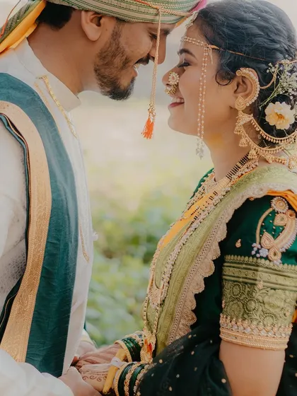 A detailed close-up focusing on the bride's traditional nath and jewelry as she looks lovingly at her groom. This shot highlights the beauty of Maharashtrian bridal details.