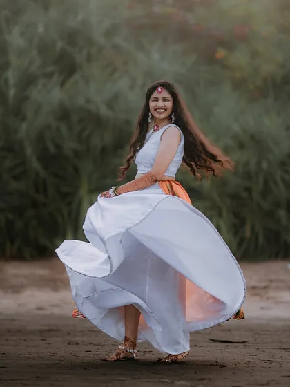 A beautiful twirling shot of the bride during her beachside Haldi ceremony, her white and orange lehenga creating a stunning visual against the natural backdrop.