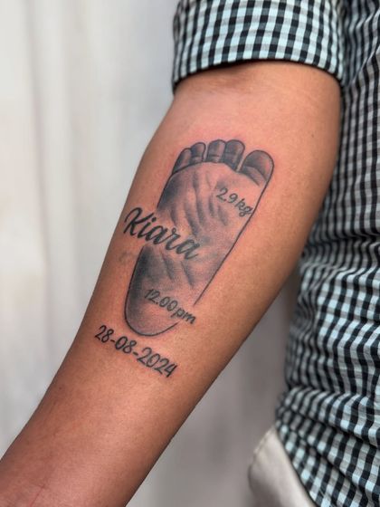 A clear, detailed shot of the baby footprint memorial tattoo on the forearm.