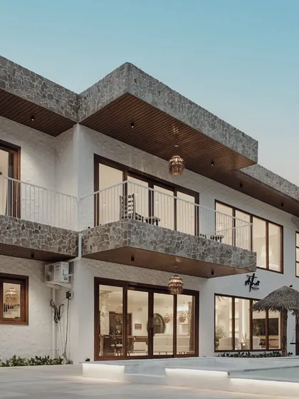 This detailed shot of the villa's facade shows the textural contrast between the rough stone cladding on the balconies and the smooth white walls. These material choices are key to achieving a modern yet rustic Balinese aesthetic.