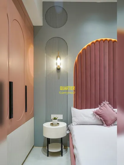 Detail shot of the wall paneling and bedside table in the daughter's room. The use of vertical fluting and geometric shapes adds texture and a modern touch to the soft color scheme.