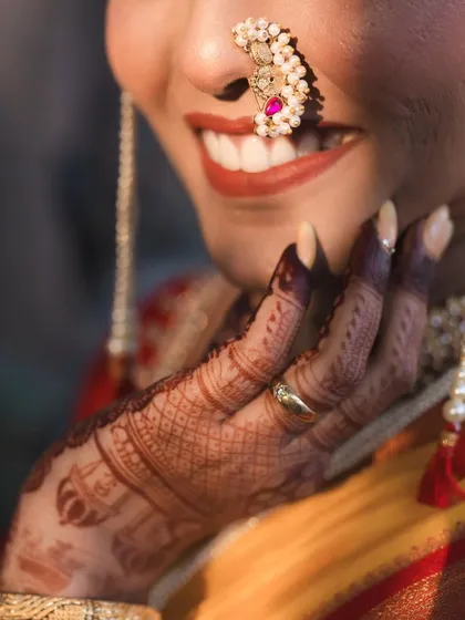 A close-up on the details: the beautiful smile, the traditional nath, and the intricate mehndi design. These shots celebrate the artistry of the bridal preparation.