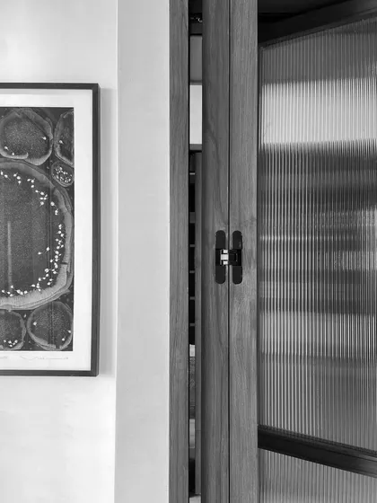 A detail from an interior project, showing a framed artwork next to a door with fluted glass. The glimpse through the textured glass creates a sense of mystery and depth, turning a simple door into a visual feature.