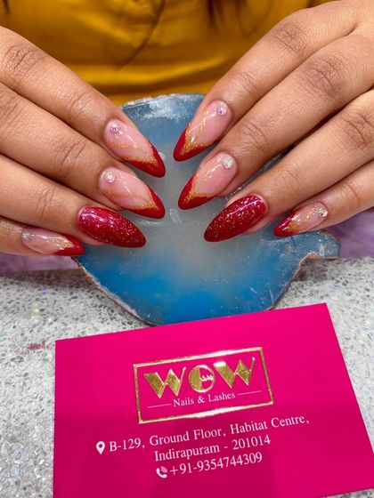 A bold and glamorous look featuring long, almond-shaped extensions with sparkling red glitter and a reverse French tip. This design is perfect for making a statement.