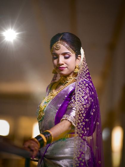 A beautiful portrait of a bride in a silver and purple saree. The makeup features a dramatic purple smokey eye to match her veil and blouse.