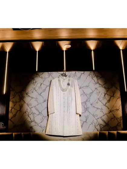 A detail shot of the groom's sherwani and necklace, artistically hung against a lit-up wall. We believe in capturing the details that make up your wedding look.
