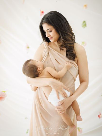 A portrait of serene motherhood. The mother gazes down at her newborn with pure love, wrapped in a flowing gown that adds a touch of goddess-like elegance.