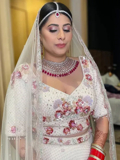 A beautiful bride in her white and ruby embroidered lehenga. The makeup is soft and subtle, with a focus on rosy tones to match the floral details of her outfit.
