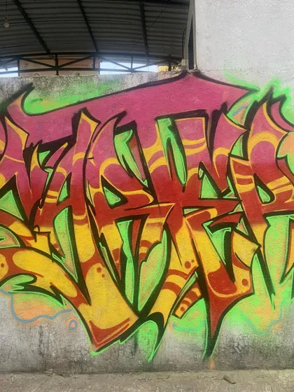A classic wildstyle piece in red, yellow, and green. The letters are sharp and interconnected, with a bright green outline that makes it jump off the concrete wall.