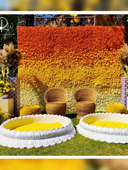 A stunning Haldi backdrop made entirely of marigolds in shades of orange and yellow, creating a beautiful ombre effect. The wicker seating and lotus-shaped basins for turmeric paste complete the traditional yet stylish look.