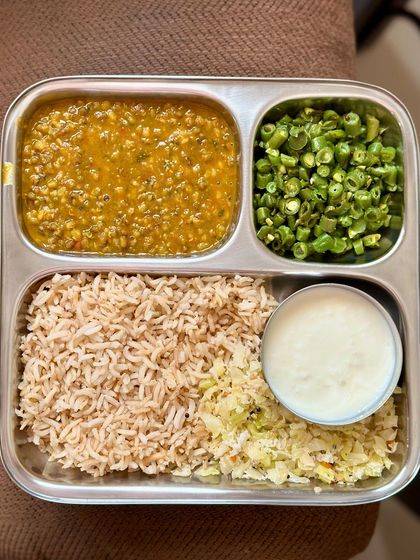 This plate features brown rice, whole green gram dal, sautéed beans, and cabbage, with a side of curd. A simple, fiber-rich meal.
