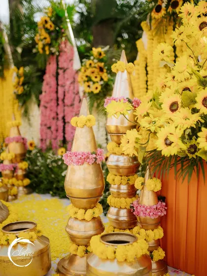 A detail shot showing the mix of textures and colors. The vibrant sunflowers and marigolds are balanced with soft pink floral accents and the warm glow of the brass pots.
