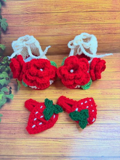 This sweet little set includes a pair of crochet baby shoes with bright red rose details and a matching pair of strawberry hair clips. Everything is made from soft yarn, perfect for a baby's comfort.