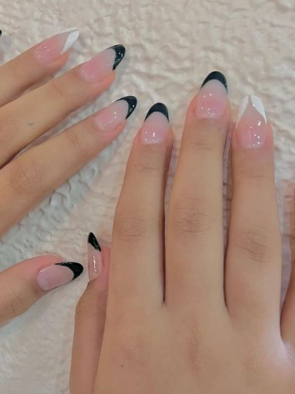 A chic twist on a classic. This look features sharp, almond-shaped nails with a mix of black and white French tips for a modern, high-contrast manicure.