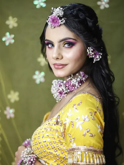 A portrait of the finished Haldi look. The hairstyle is an elegant braided updo, perfect for keeping the hair neat while allowing the floral jewelry to be the centerpiece.