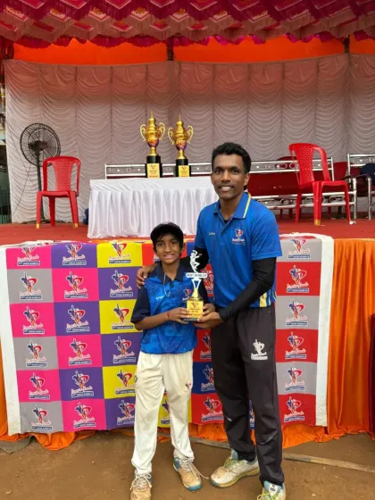 A young cricketer from the U-10 tournament proudly accepts his trophy from one of our senior coaches in front of the academy banner.