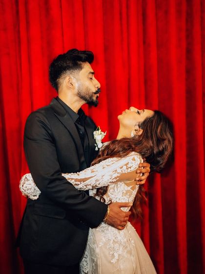 A playful and dramatic pose against a rich red curtain. This creative couple portrait adds a touch of theatrical flair to the wedding album.