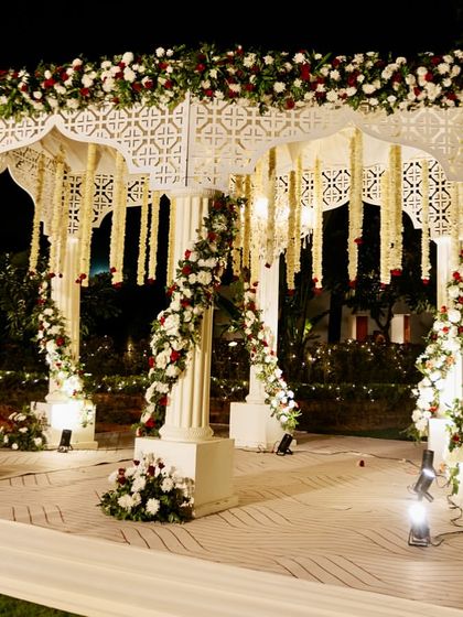 A beautiful white mandap decorated with classic red and white roses and hanging tuberoses, creating a timeless and elegant look for a night wedding.