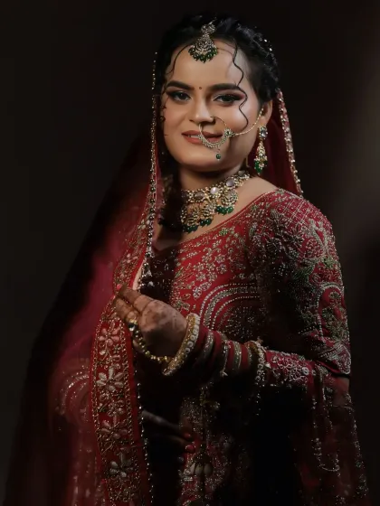 A classic portrait of a bride in a deep red outfit. The lighting accentuates her flawless makeup and the elegance of her pose.