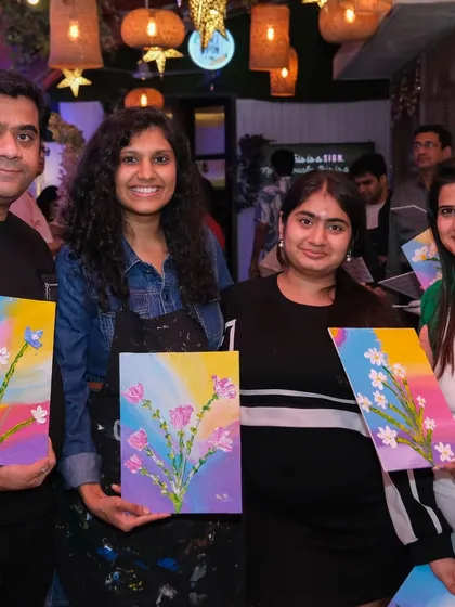 A group of friends poses with the floral canvas paintings they created during a private party. It's a wonderful way to celebrate and make memories together.