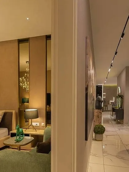 A view from the bedroom into the hallway of a luxury apartment. The lighting design uses a combination of a decorative chandelier inside the room for ambiance and a sleek magnetic track system in the corridor for functional, modern pathway lighting.