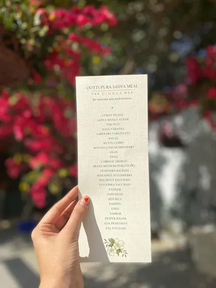 Holding up the Sadya menu against a backdrop of bougainvillea, showcasing the care and detail we put into every aspect of the event.