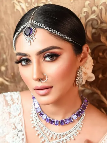 A frontal view of the elegant bridal look. The sleek bun ensures that all the attention is on the client's face, her beautiful jewelry, and her striking makeup.