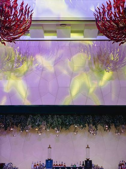 The bar area for this modern reception was designed to be a statement piece. A canopy of hanging greenery and lights is set against a textured wall, with the venue's red chandeliers adding a pop of color.