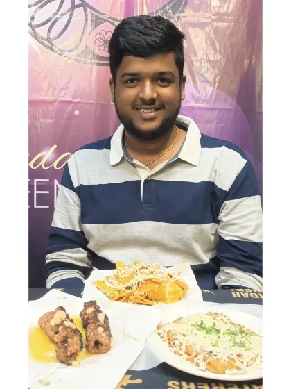 A happy guest with a table full of our delicious food, including seekh kebabs and tawa specials.