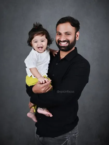 A father holds his laughing child in his arms. This simple portrait against a dark background beautifully captures a moment of pure joy and connection.