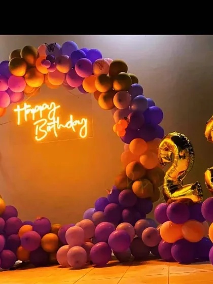 A bold and colorful 23rd birthday decoration. The circular balloon arch in shades of purple and orange is paired with gold foil number balloons for a fun and energetic vibe.