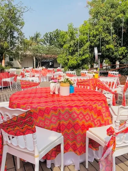 The guest seating area for a vibrant Haldi, with tables covered in colorful traditional prints and chairs tied with 'bandhani' fabric.