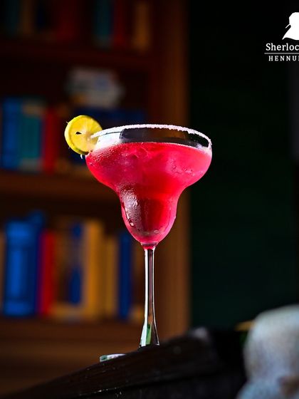 A vibrant pink margarita with a salted rim, set against our library-themed wall. It's a perfect mix of classy and fun.