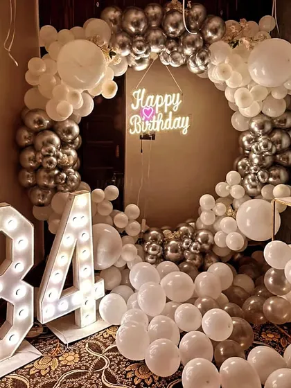 A glamorous white and silver theme for a 34th birthday. This decoration features a full balloon ring, a neon sign, and large marquee numbers, creating a luxurious and celebratory feel.