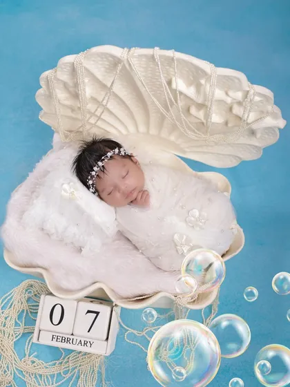 Another angle of our popular pearl-in-a-shell newborn setup. This image highlights the intricate details of the prop and the peaceful slumber of the baby, with a calendar block to mark the special day.
