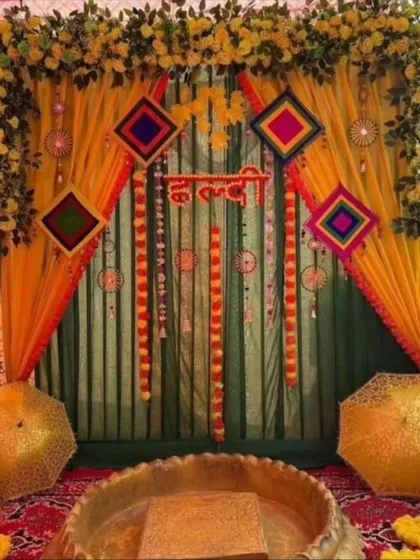 A traditional Haldi ceremony setup with a brass urli for the ritual. The backdrop is created with yellow and green drapes, marigold garlands, and colorful hangings, perfect for home-based celebrations.