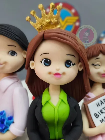 A close-up of the "Super Girl" mom figurine, crowned and seated between her husband and daughter. The details in the custom outfits were based on specific client requests.