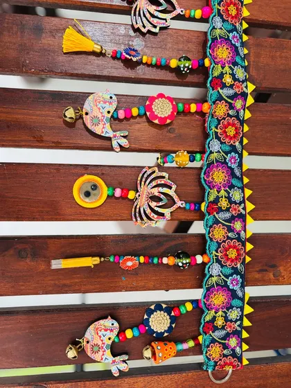 A detailed shot of the 'Tamaara' toran, showing the mix of my original artwork on wooden cutouts, metal buttons, and soft tassels.