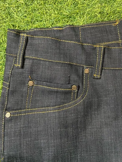 Detail of the front pocket on a pair of custom raw denim jeans, showing the clean, strong stitching and classic rivet hardware.